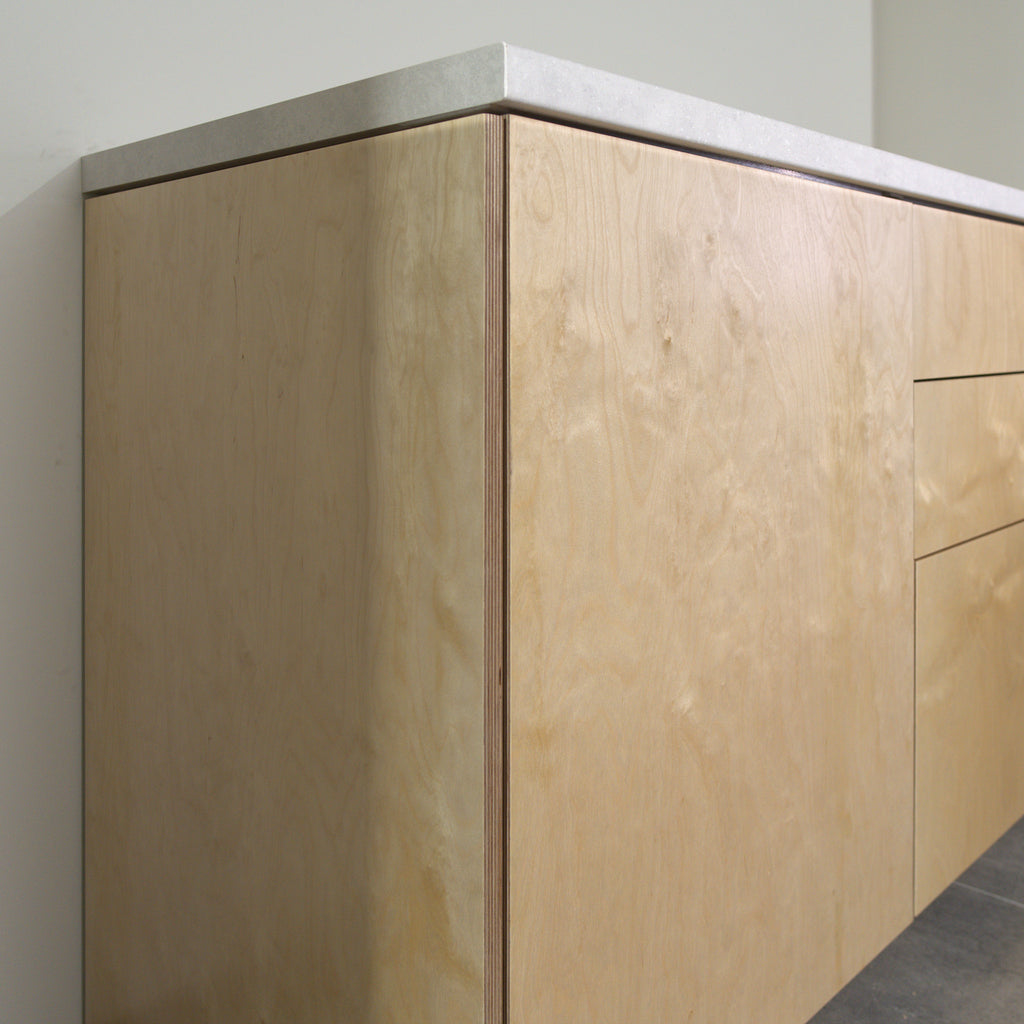 Corner of a cabinet with birch plywood fronts and side panel, angled view from the left